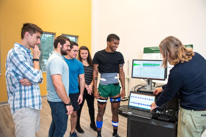 Students gathered around a machine monitoring a student's vitals listening to the professor explain the purpose of the system